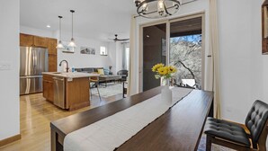 Una cocina moderna con electrodomésticos de acero inoxidable, un comedor con una mesa larga y vistas a través de un vano.