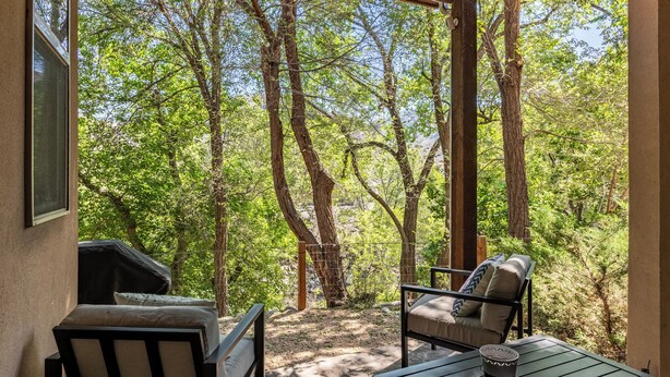 Un patio exterior con mesa y sillas, una parrilla y vistas a un área boscosa.