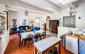 A spacious living area with a dining table, blue sofas, and a kitchen area with a refrigerator and cabinets.