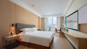 A hotel room with a bed, bedside table, chair, desk, and a large window with a city view. - Muwang Hotel Dalian (Dalian)