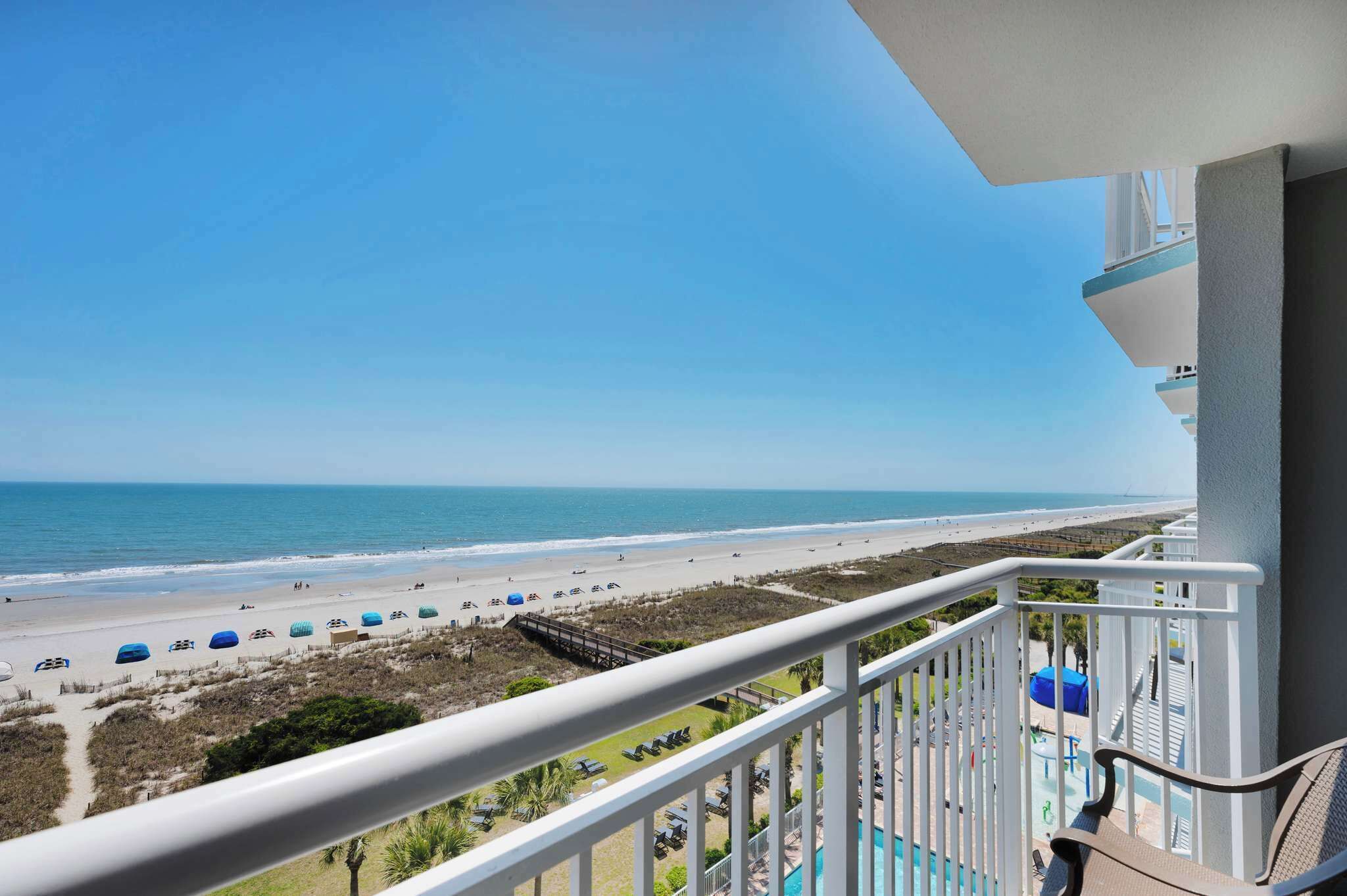 Ein Balkon mit Blick auf den Strand, ein Poolbereich und ein klarer Himmel.