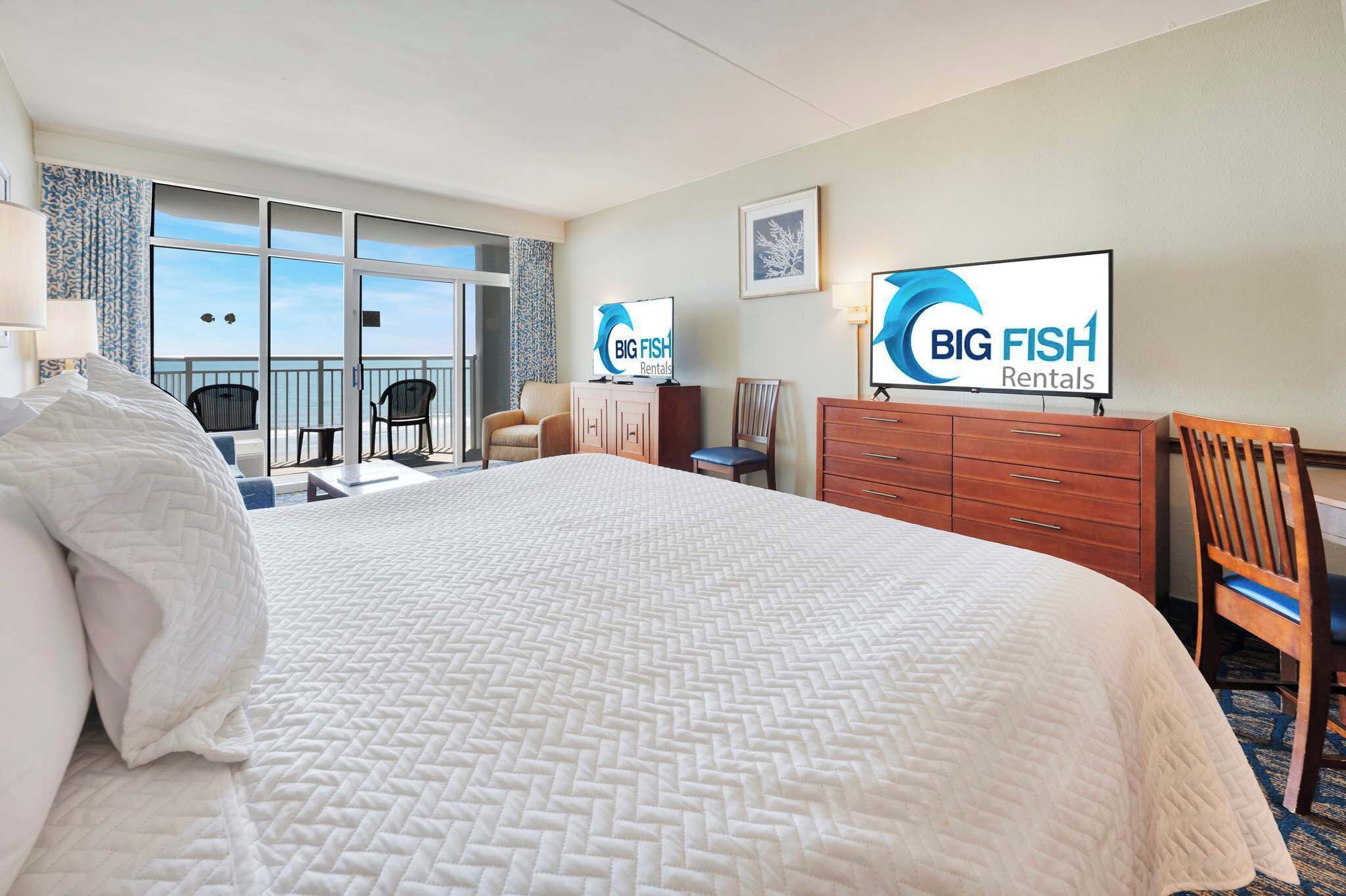 Ein Hotelzimmer mit einem großen Bett, einem Fernseher, einem Schreibtisch und Blick auf den Balkon.