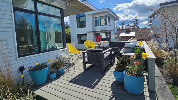 A modern house with a deck, large windows, and outdoor furniture.