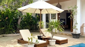 A poolside area with lounge chairs, a large umbrella, and potted plants. - Villa Mango (Kuta)
