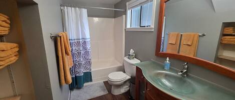 Et badeværelse med vask, toilet, brusebad og spejl.