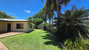 A single-story house with a well-maintained lawn, a small porch, and tall palm trees.