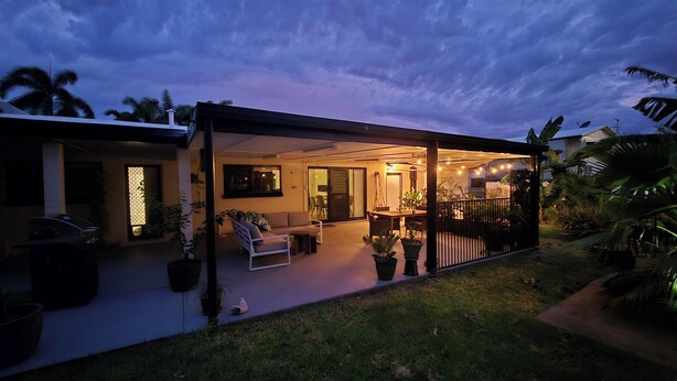 A covered outdoor patio with a dining area, seating, and potted plants.