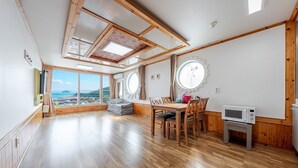 Una habitación amplia con suelo de madera, una mesa de comedor con sillas, microondas y vista al mar.