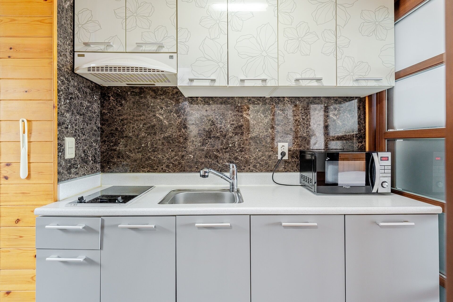 A kitchen with a granite backsplash, white cabinets, a stainless steel sink, and a microwave.