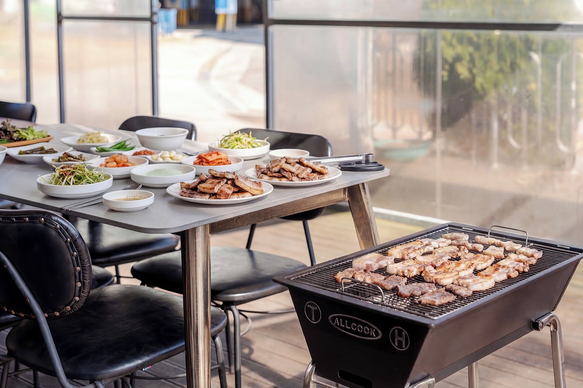 A barbecue grill with skewers of meat, a table with various dishes, and outdoor seating.