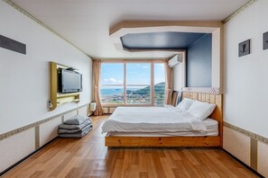 A hotel room with a large bed, a television, a view of the city, and a balcony.