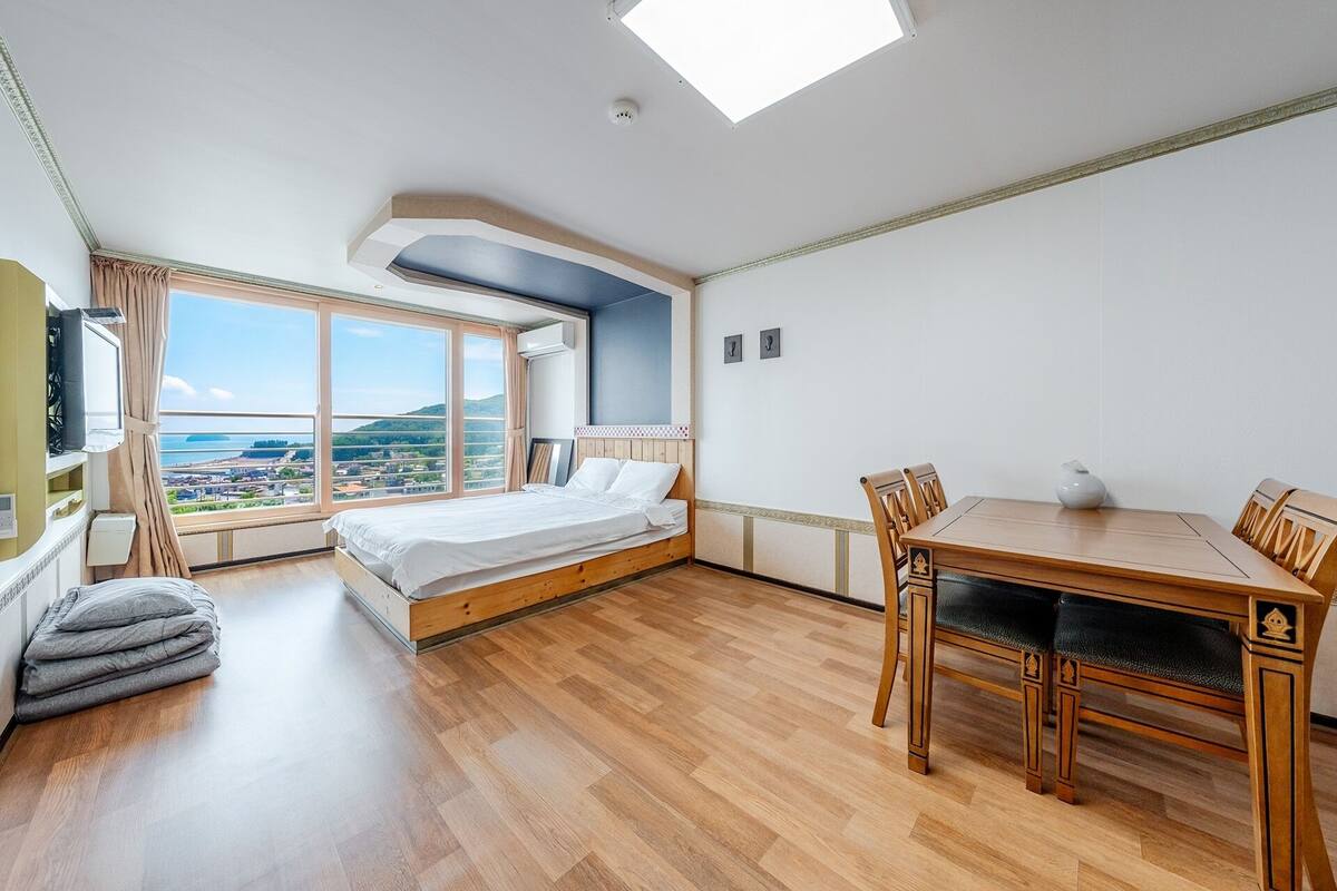 A bedroom with a bed, a dining table, and a view of the city.