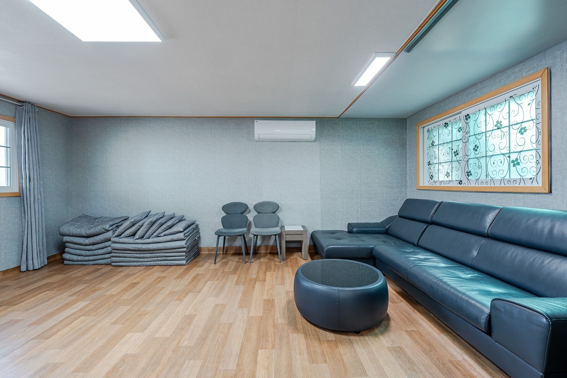 Un salon moderne avec un canapé, un pouf, des fauteuils et une pile de couvertures pliées.