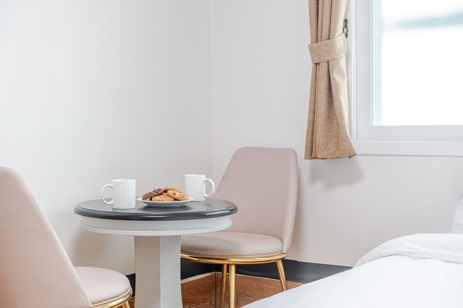 Una habitación de hotel con una mesa redonda, dos sillas, una cama y una ventana con cortinas.