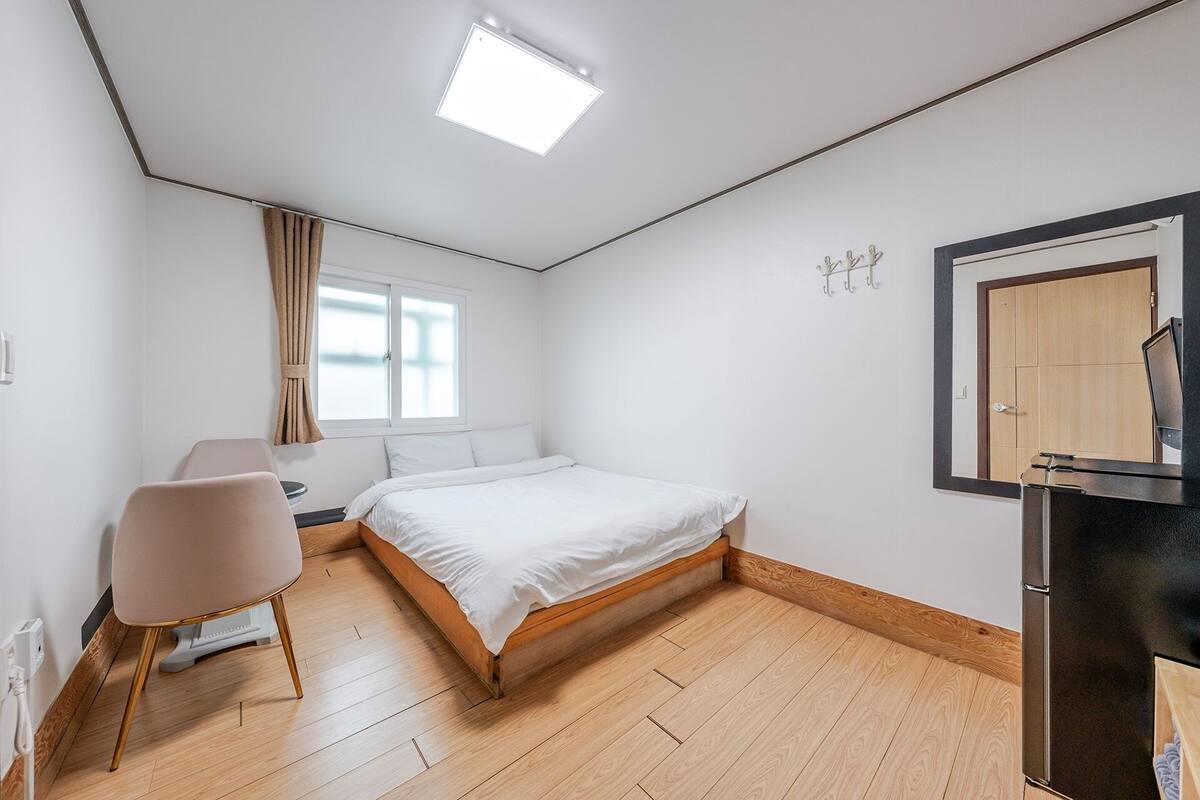 A bedroom with a bed, a chair, a desk, a mirror, and a window with curtains.