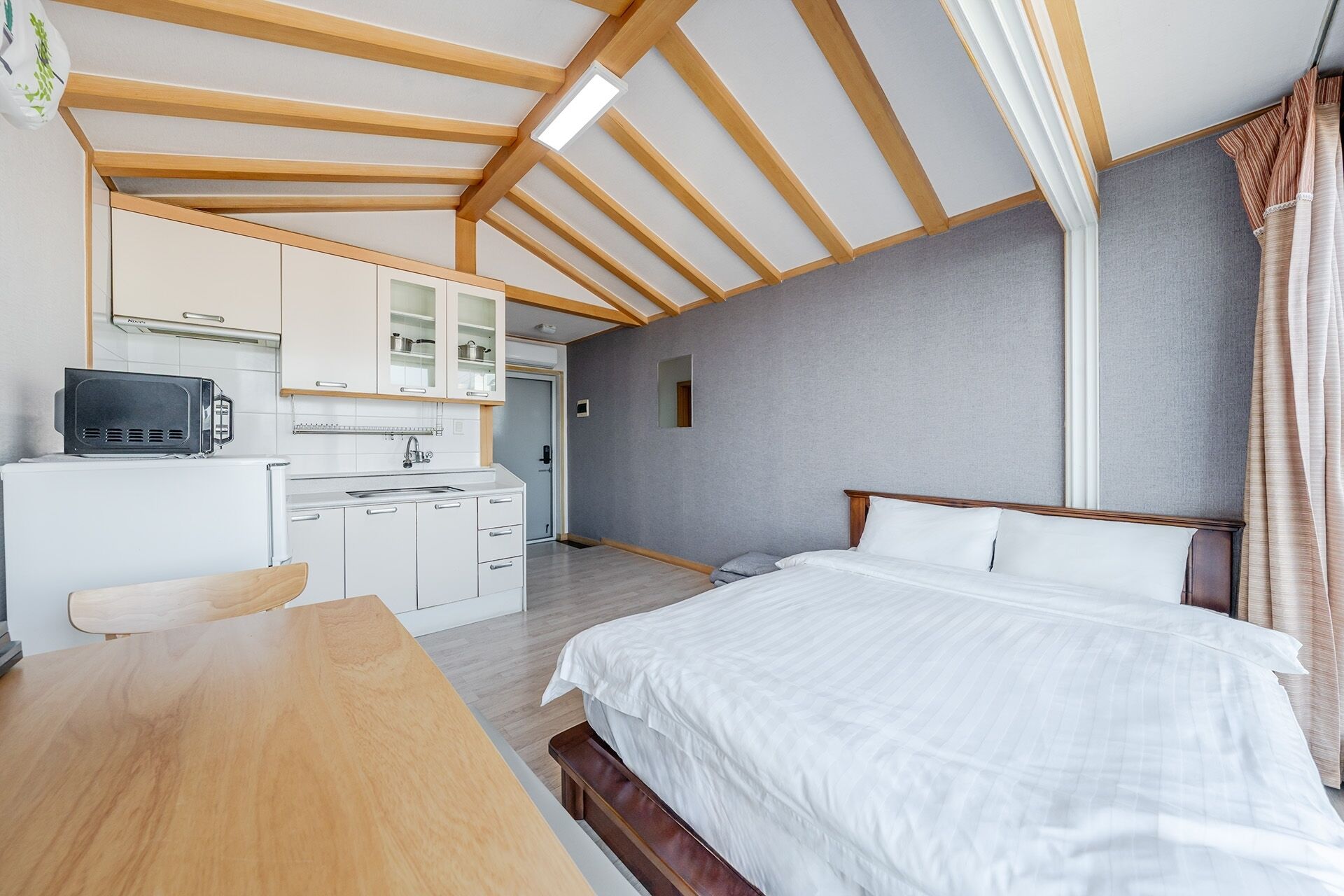 Una habitación pequeña con cama, kitchenette y techo de madera.