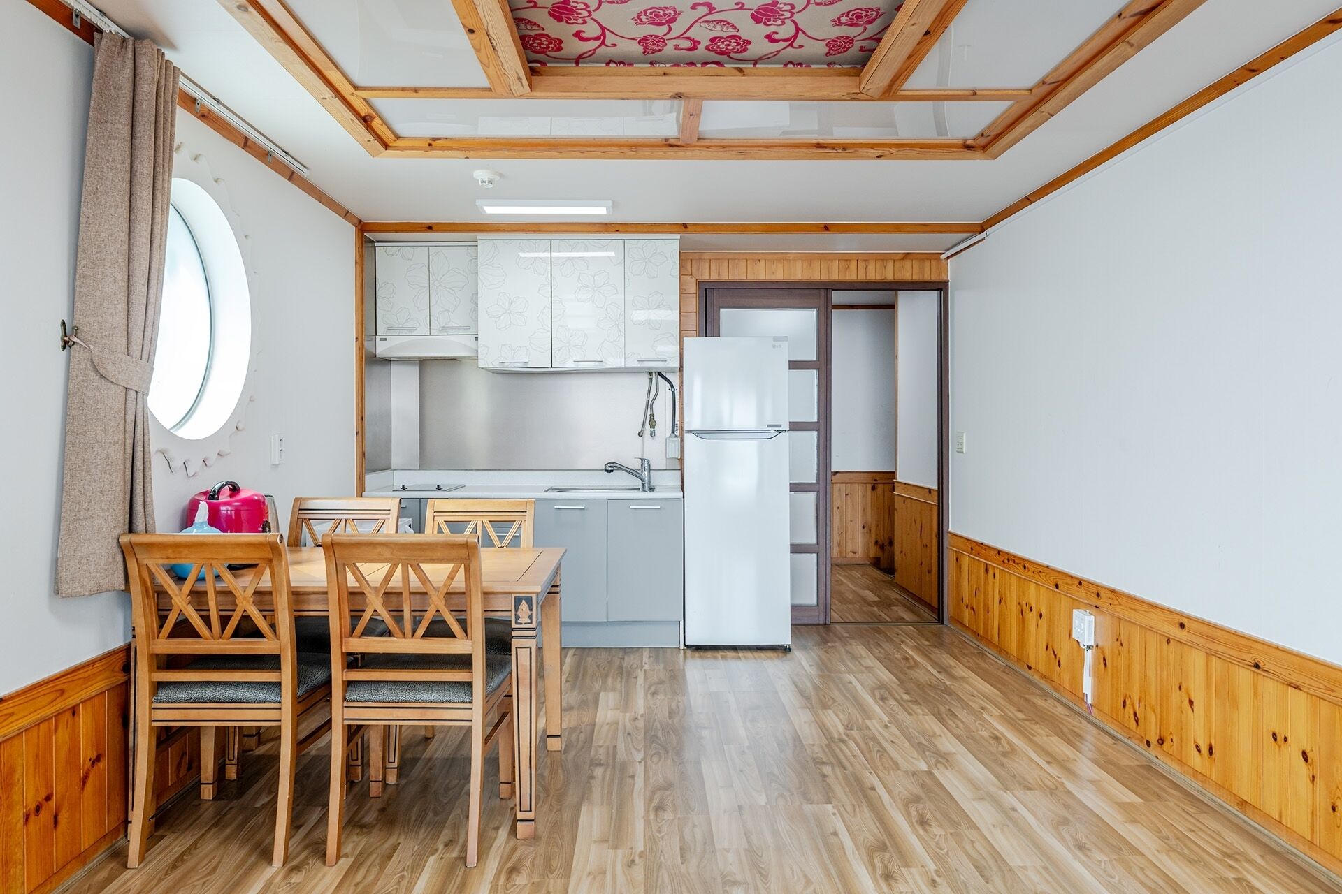 Une cuisine de taille réduite, dotée de meubles en bois, d’un réfrigérateur blanc et d’un coin repas avec des chaises et une table en bois.
