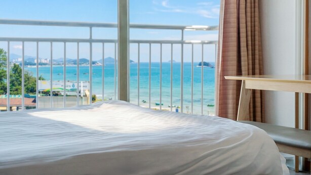 Habitación de hotel con cama, una mesita, vista al mar y barandilla de balcón.