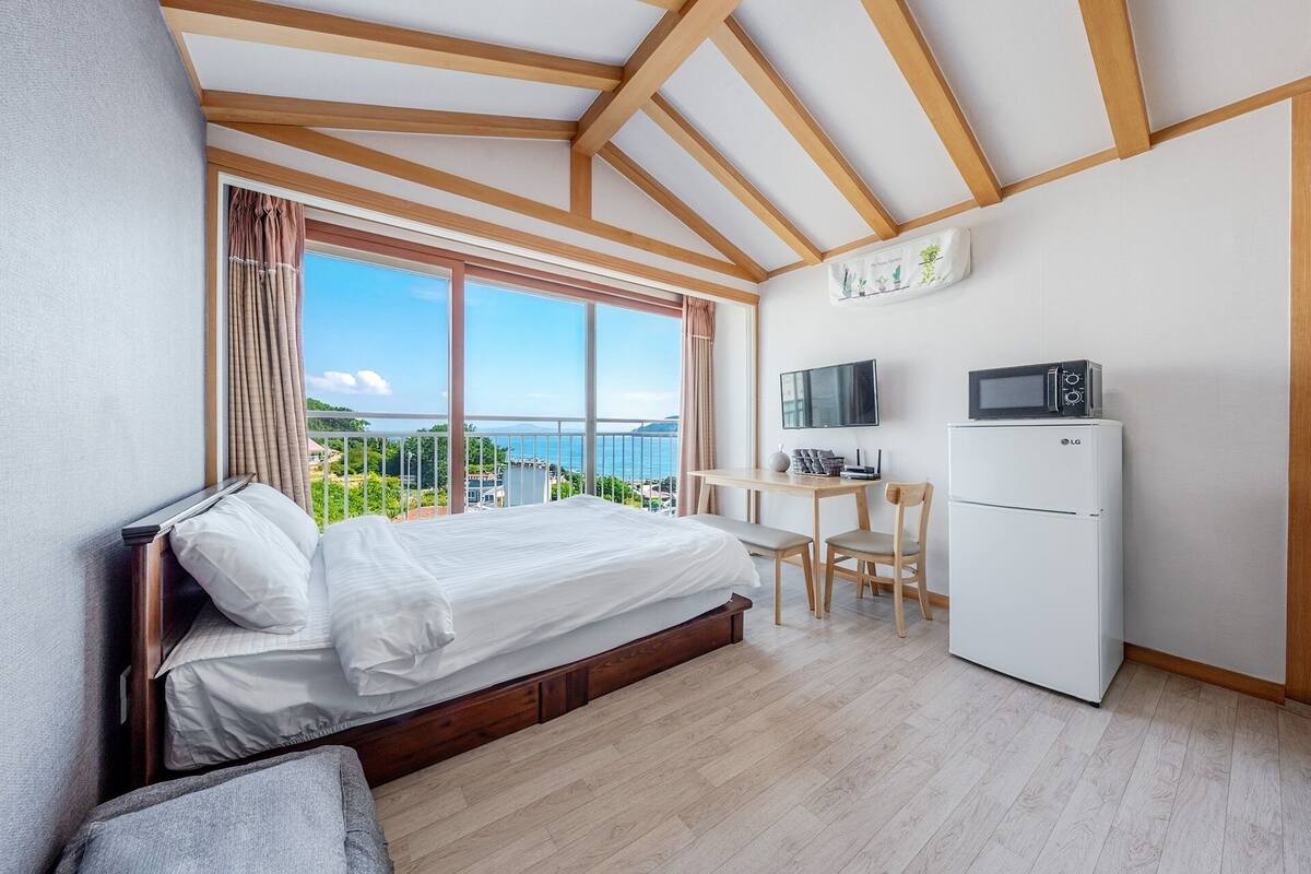 A bedroom with a bed, a desk, a chair, a TV, a microwave, and a refrigerator.