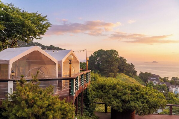 A cabin with a glass enclosure and a wooden deck, overlooking a coastal landscape. - Muuido Haedungsil Pension (Incheon)
