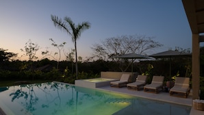Ein Pool mit Liegestühlen und Sonnensegel, umgeben von Bäumen und Pflanzen.