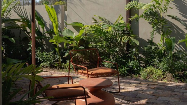 Ein Außenbereich mit Tisch und Stühlen, umgeben von üppigem Grün und einem Gebäude mit Balkon.
