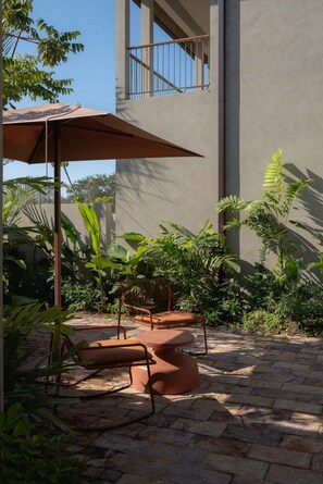 Ein Außenbereich mit Tisch und Stühlen, umgeben von üppigem Grün und einem Gebäude mit Balkon.