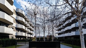 Un edificio residenziale moderno con numerosi balconi, un'area verde centrale e cielo sereno.