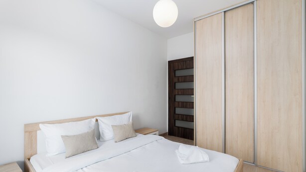 Una camera d'albergo moderna con un letto in legno, lenzuola bianche, un armadio in legno e un comodino.