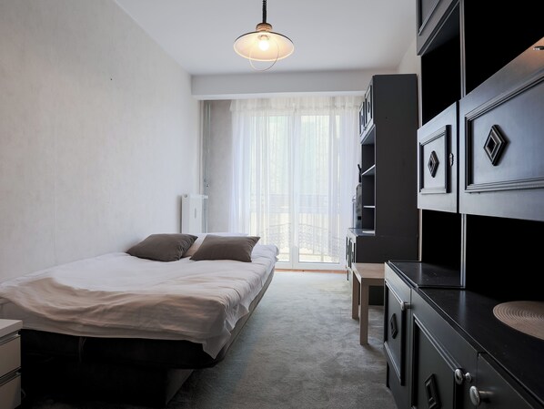 A hotel room with a bed, a desk, a wardrobe, and a view of the outdoors. - Fałata Comfort Apartment (Toruń)