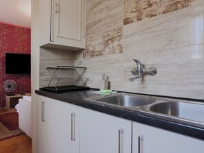 A kitchen with two sinks, a microwave, a fan, and a tiled backsplash with cityscape designs. - Fałata Comfort Apartment (Toruń)