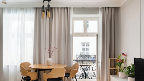 Un coin repas avec une table ronde et des chaises, un téléviseur posé sur un meuble, et un balcon doté d’une balustrade.