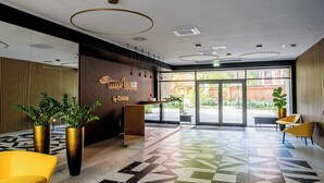 A modern lobby with a geometric patterned floor, a reception desk, and yellow chairs. - Modena Jeżyce Deluxe Apartment (Poznań)