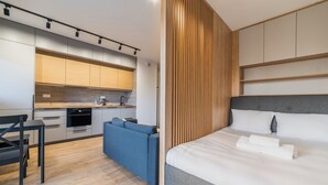 A modern hotel room with a bed, a sofa, a kitchenette, and a wooden accent wall. - Modena Jeżyce Deluxe Apartment (Poznań)