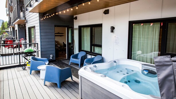 Un balcon avec un jacuzzi, des chaises bleues et une poussette.