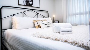 Un lit bien fait, avec une literie blanche, une tête de lit en métal noir et un tableau représentant une vache accroché au mur.
