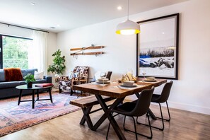Ein Essbereich mit Holztisch, Stühlen und einer Pendelleuchte. Im Wohnbereich befindet sich eine Couch und ein Couchtisch mit Teppich.
