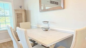 Un coin repas avec une table blanche, des chaises en osier et un miroir au mur.