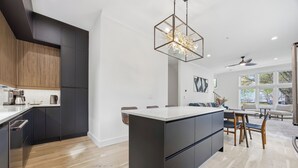 A modern kitchen with dark cabinetry, a central island, and a dining area with a ceiling fan and large windows. - Steps to Mercedes Benz, Arena, GWCC, Rooftop view (Atlanta)
