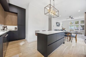 Eine moderne Küche mit dunklen Schränken, einer zentralen Kochinsel und einem Essbereich mit Deckenventilator und großen Fenstern.