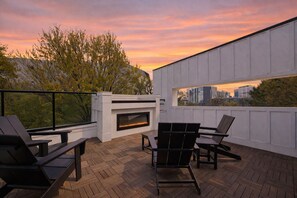 Eine Dachterrasse mit Kamin, Sitzgelegenheiten im Freien und Blick auf die Skyline der Stadt bei Sonnenuntergang.