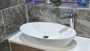 Une salle de bain avec un lavabo sur colonne blanc, des murs en marbre et un meuble en bois.