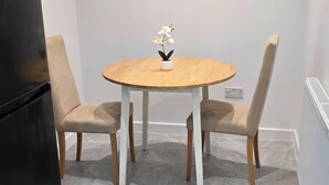 Un coin repas avec une table ronde en bois, deux chaises beiges et une orchidée blanche dans un pot.