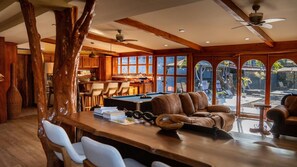 A spacious room with a pool table, leather chairs, wooden beams, and large windows overlooking a pool area. - Villa Hakomar Private Pool & Game Room – Walk to Beach & Downtown Jacó (Jaco)