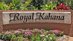 Een bord met de tekst 'Royal Kahana', omgeven door kleurrijke bloemen en planten.