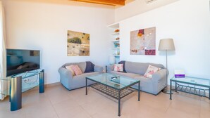 Una sala de estar con televisión, sofá, mesa de centro de vidrio y obras de arte en las paredes.