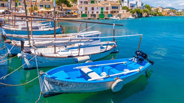 Un puerto deportivo con varias embarcaciones amarradas, un cielo azul despejado y edificios al fondo.
