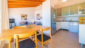 Una cocina moderna con armarios blancos, un refrigerador de acero inoxidable y un comedor con mesa y sillas de madera.