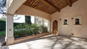 Ein überdachter Patio-Bereich mit Fliesenboden, Holzbalken und Blick auf den Garten.