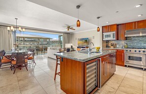 A modern kitchen with a large island, stainless steel appliances, and a dining area with a view. - Maui Resort Rentals: Honua Kai – 6 Bedroom Retreat, Over 4000 Combined Sq Ft, Stunning Premier Ocean Views! (Lahaina)